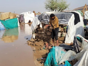Una personas sacando agua de un alojamiento temporal en medio de un asentamiento inundado.