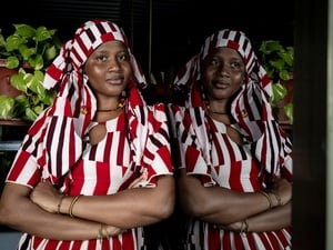 Una mujer de Burkina Faso, que lleva puesto una indumentaria de color blanco y rojo, mira a la cámara con los brazos cruzados sobre su abdomen