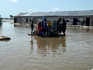 Un grupo de personas intentan acceder a una fuente de agua potable, en medio de un paisaje inundado.