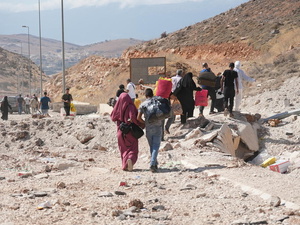 Varias personas transportan sus pertenencias por una carretera llena de escombros y colinas a ambos lados