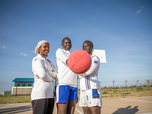 Tres mujeres juntas en una cancha de básquetbol, una con una pelota en la mano
