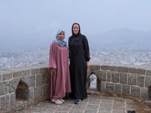 Dos mujeres posan juntas para una foto en un punto panorámico de una ciudad.
