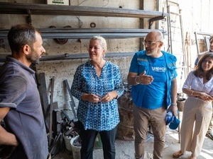 Dos mujeres y dos hombres de pie conversando. Un hombre viste playera y chaleco de ACNUR azul