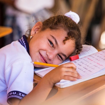 En una escuela en Colombia, una niña sonríe mientras se recuesta sobre su libreta en un aula.