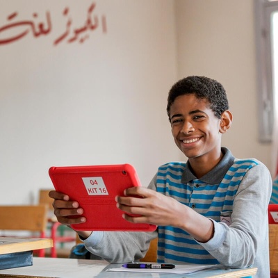 Un chico en Egipto sostiene una tableta mientras sonríe para la cámara.