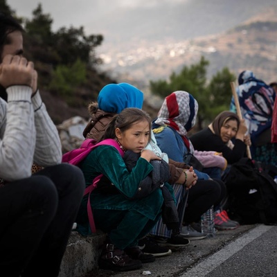 Mujeres, hombres, niñas y niños esperan al lado de la carretera en Grecia