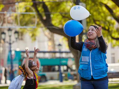 UNHCR worker and a young girl throw balloons in the air