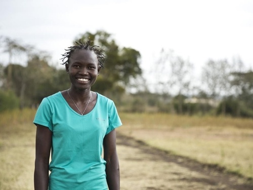 Una mujer sudsudanesa en un terreno con vegetación sonríe a la cámara