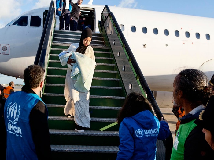 Una mujer somalí lleva a su bebé en brazos mientras sale de un avión luego de haber sido evacuada de Libia y llevada a Italia. El personal de ACNUR la saluda.