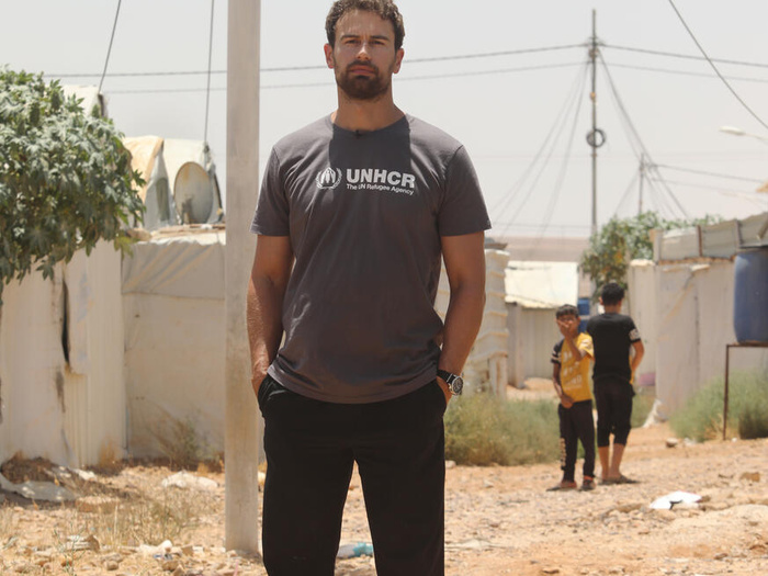 En un campamento de refugiados, un hombre con barba que lleva puesta una camiseta con el logotipo de ACNUR mira a la cámara