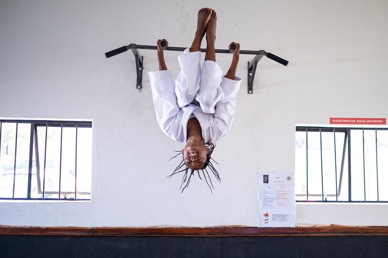 Una chica que practica judo se sostiene de cabeza de una barra que está empotrada en la pared