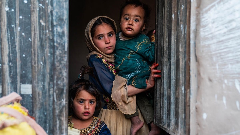 Dos niñas y un niño de distintas edades se asoman por una ventana; sus rostros muestran preocupación.