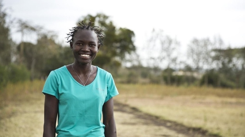 Una mujer sudsudanesa en un terreno con vegetación sonríe a la cámara