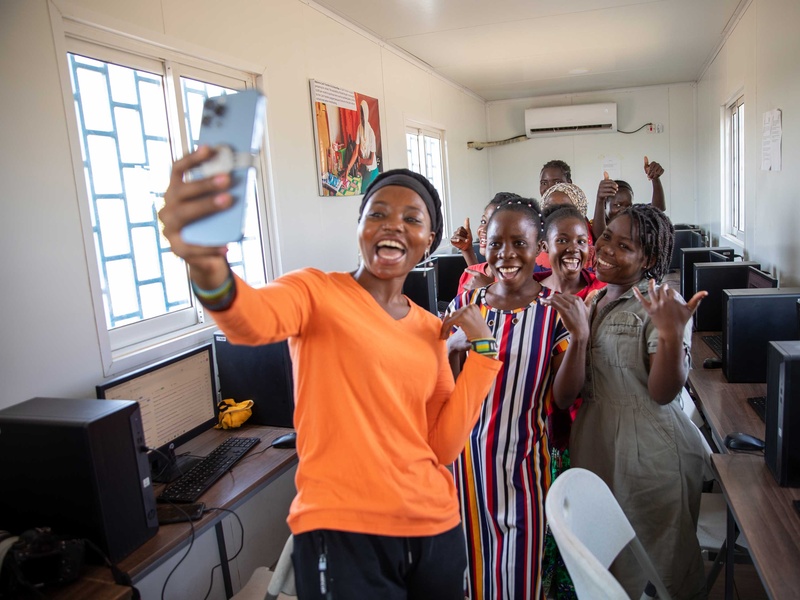 En el pasillo de un aula de computación, un grupo de mujeres se toma una selfi.