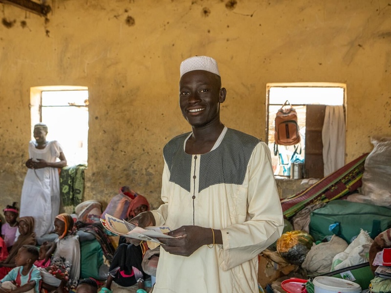 En medio de un hacinado recinto, un joven sudanés sostiene un par de documentos.