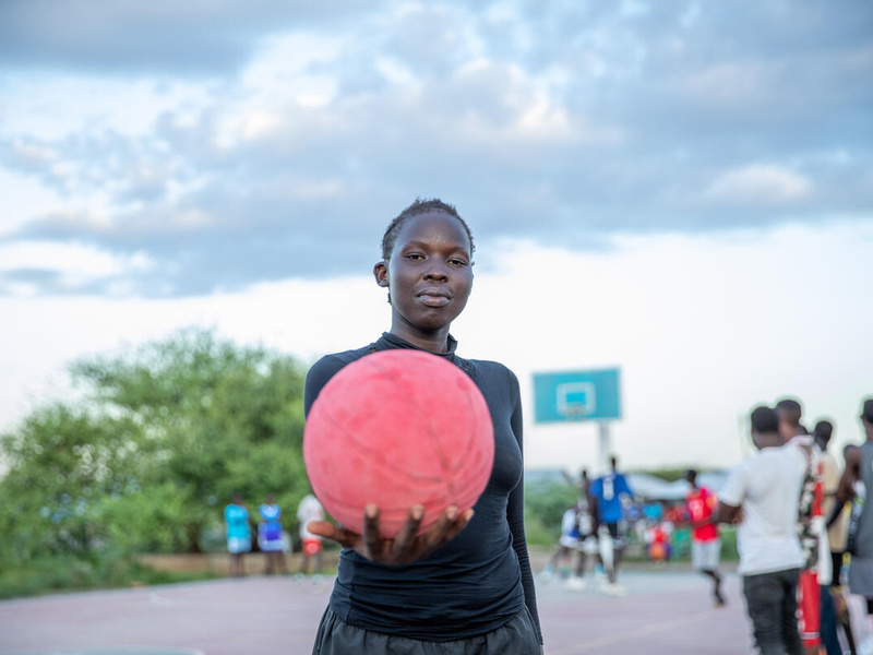 Una joven sostiene con confianza una pelota de baloncesto rosa frente a la cámara
