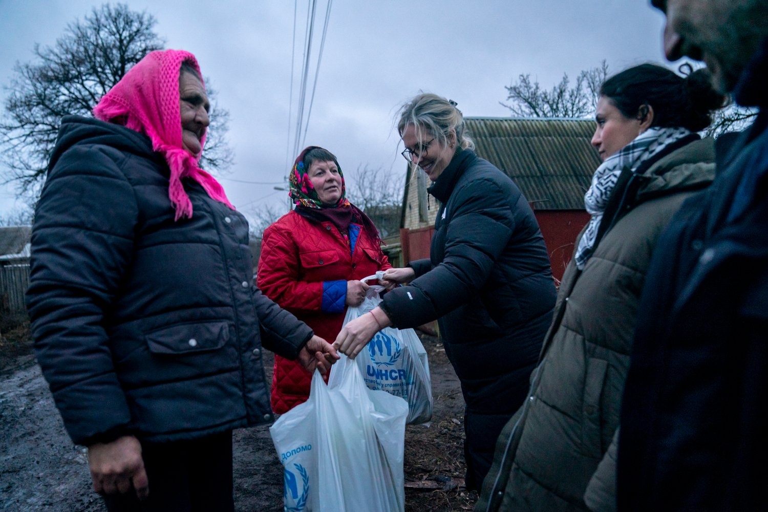 Dos mujeres ucranianas reciben bolsas de alimentos y otros artículos de ayuda de miembros del personal de ACNUR.
