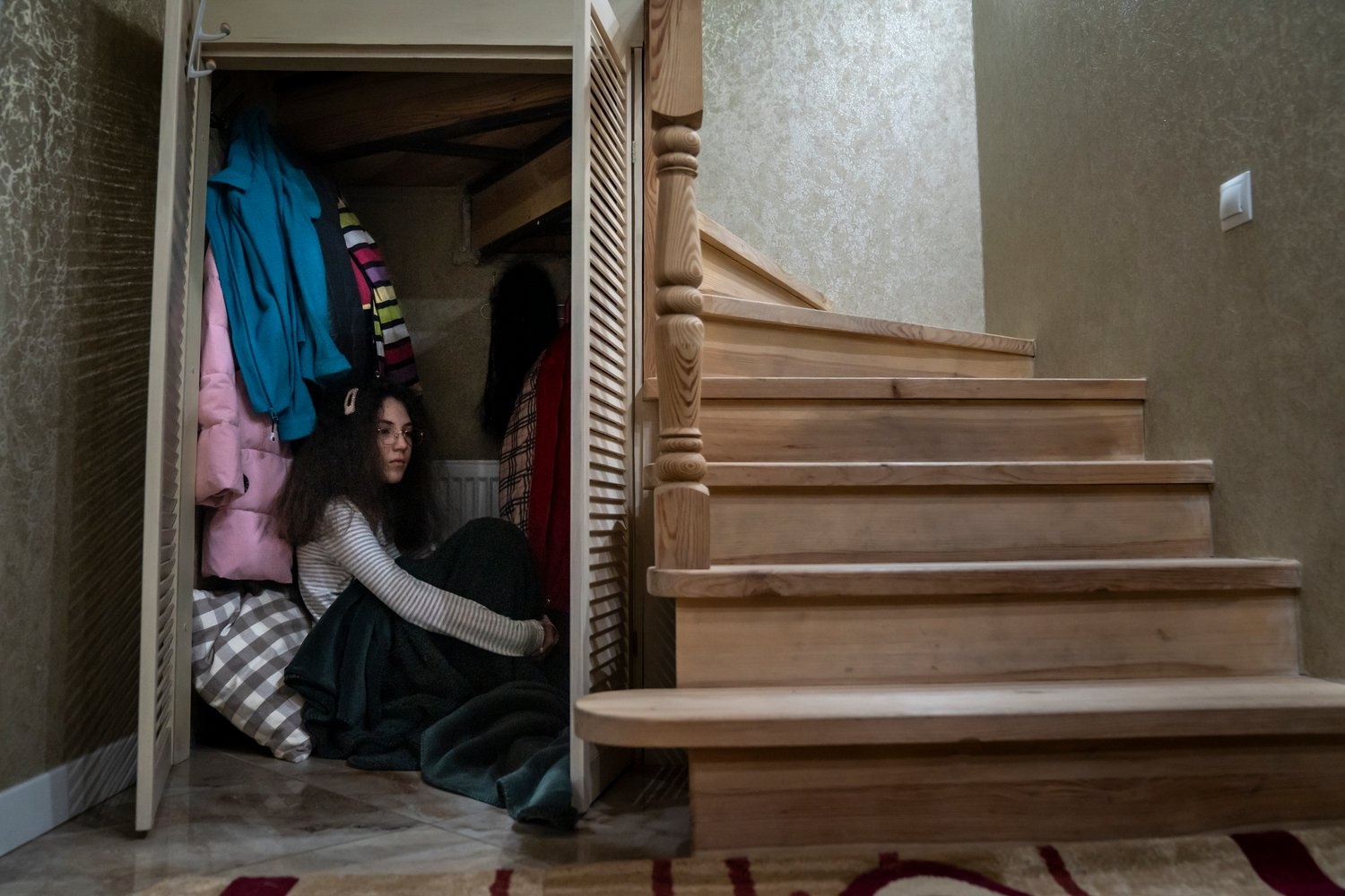 Una niña se sienta en un armario bajo la escalera de su casa.