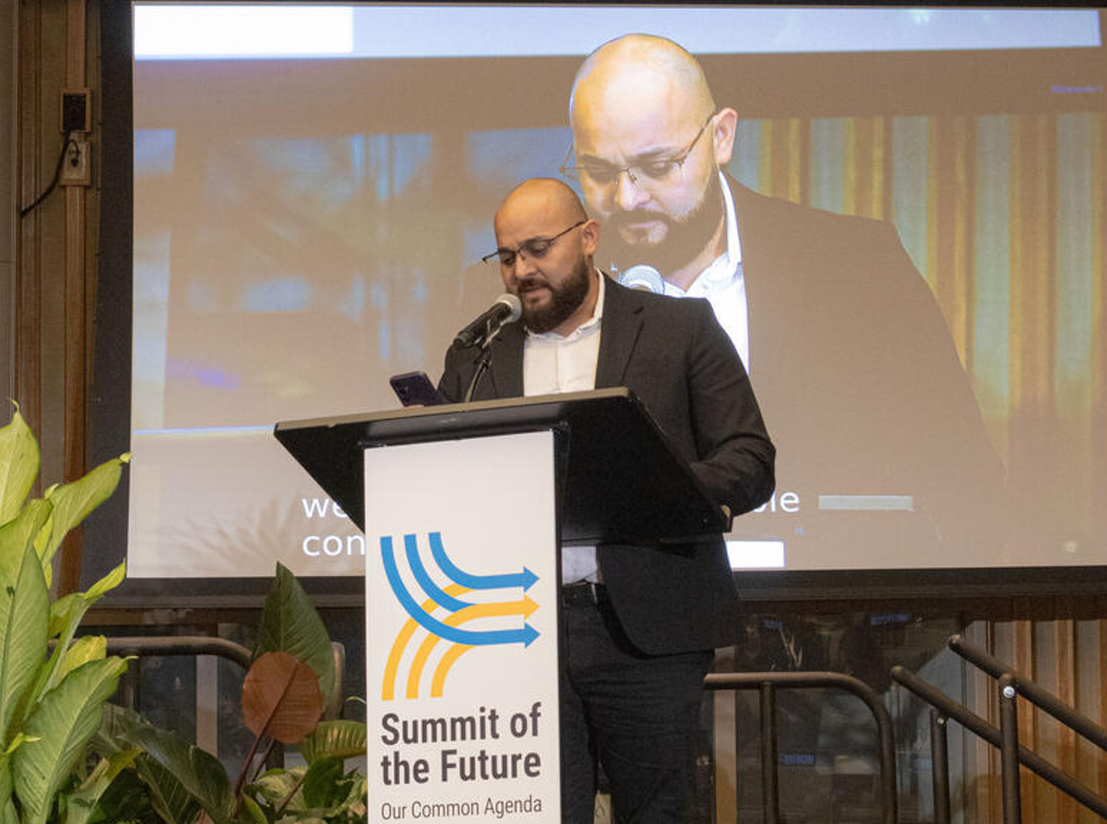 Un hombre con anteojos, que viste traje negro y camisa blanca habla sobre un podio donde se lee “Summit of the future” (cumbre del futuro) 