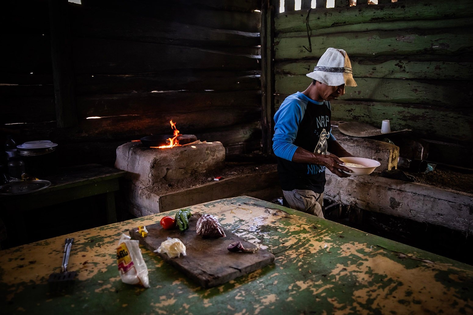 Un hombre cocina en una casa de madera con un fogón de piedra.