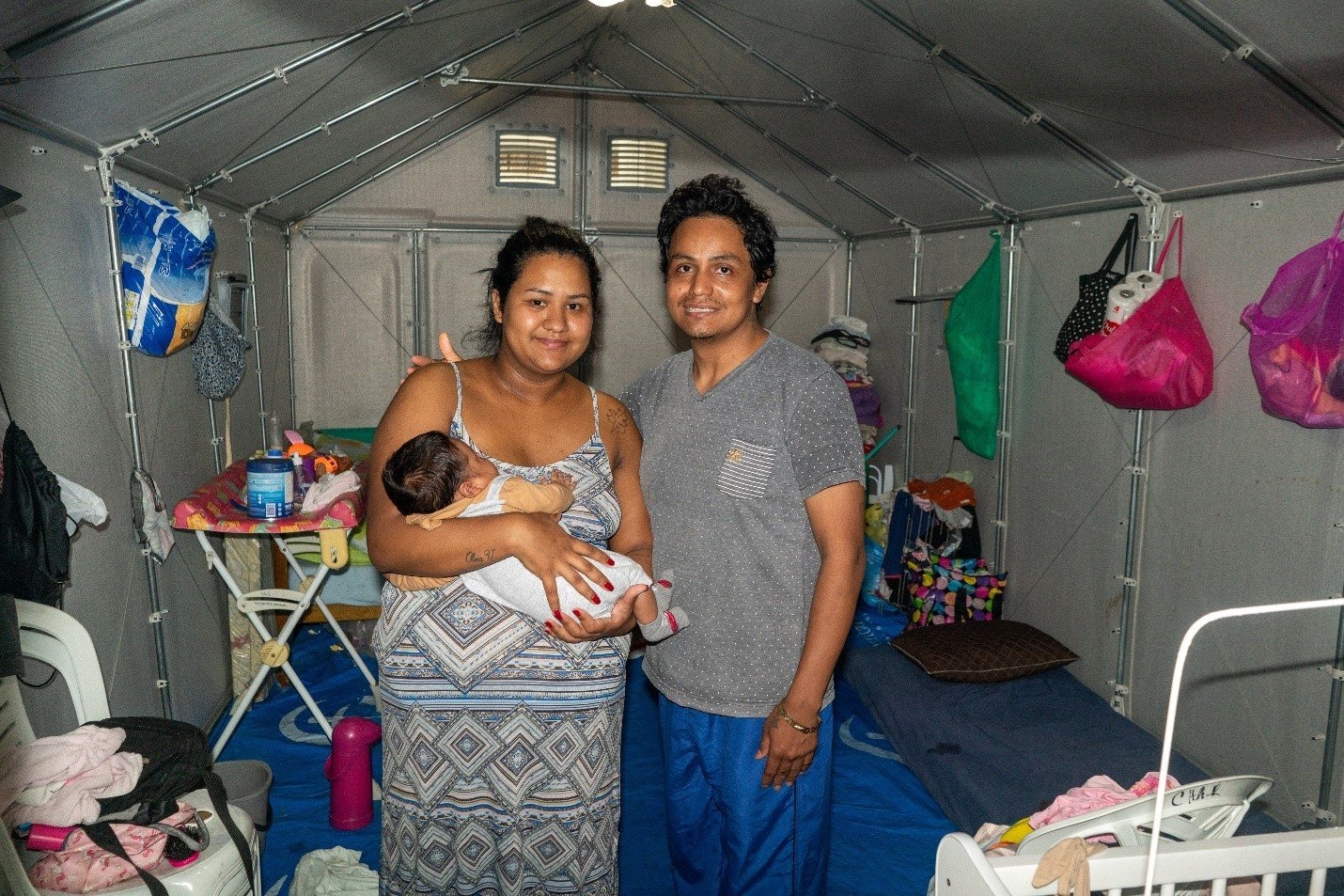 Un hobre y una muher que sostiene a un bebé posan para la foto dentro de un alojamiento prefabricado.