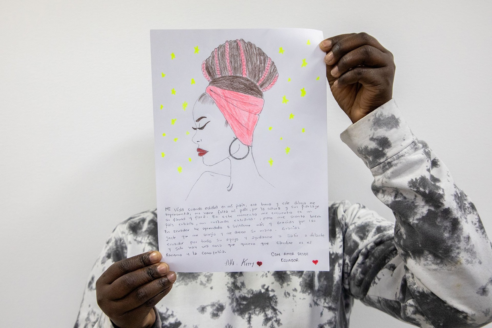 Una persona muestra una carta donde se se ve un dibujo realizado a mano. La carta cubre la cara de la persona.
