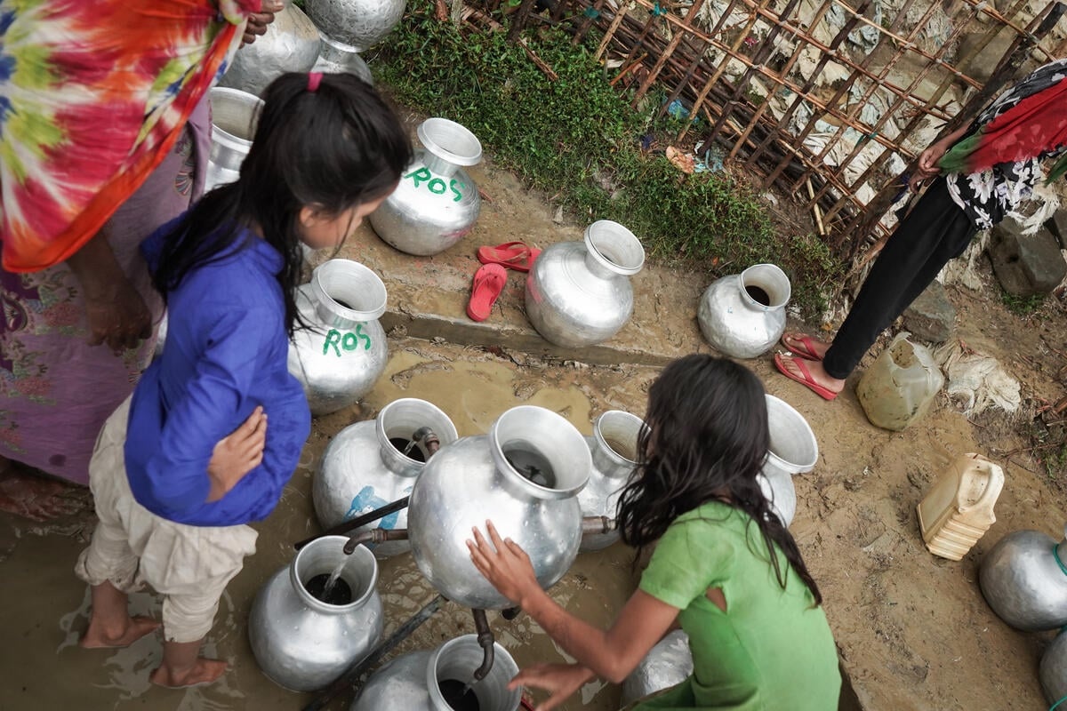 Dos niñas recolectan agua en envases plateados dispersos por el suelo