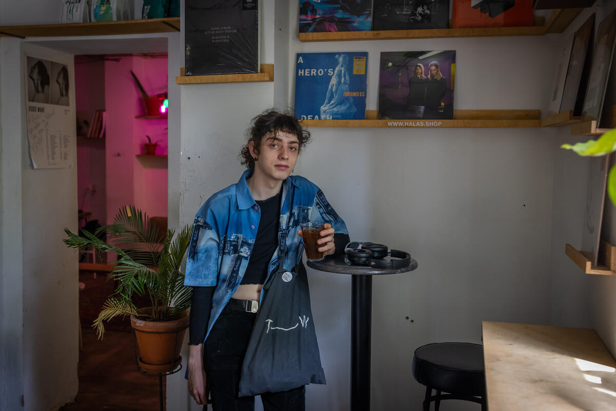 Una mujer que viste camisa azul está recargada sobre una mesa negra de un café