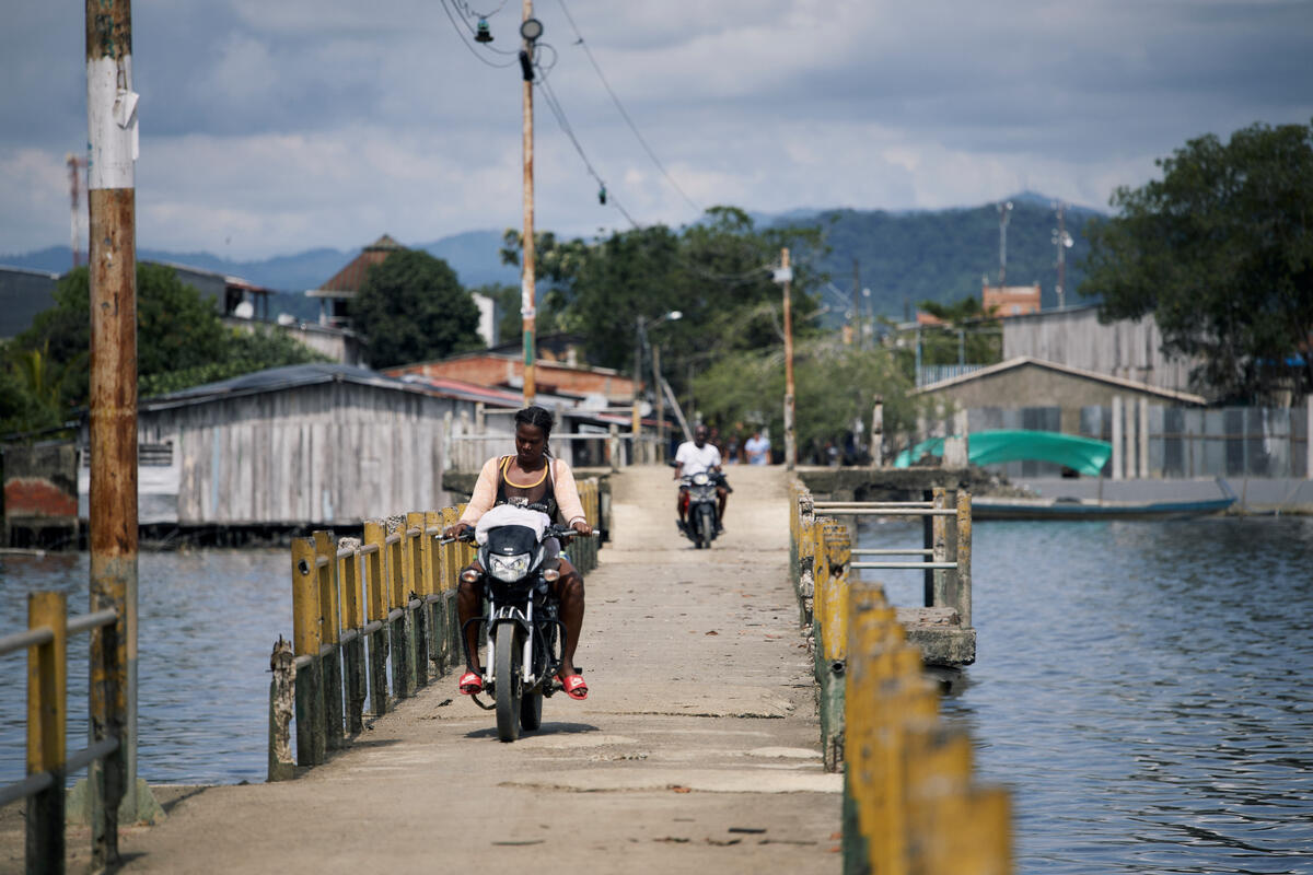 Una mujer afrocolombiana cruza una vía en un motocicleta