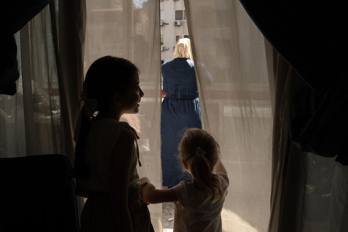 Silueta de dos niñas viendo hacia la ventana de un balcón a través de las cortinas