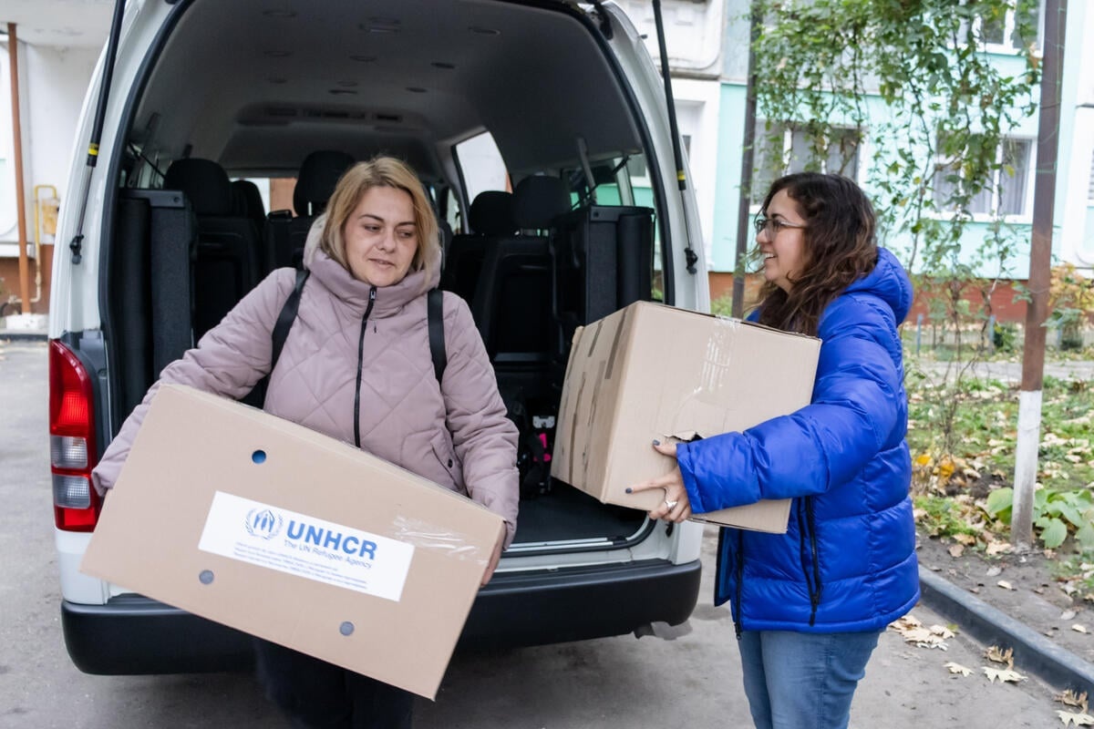 Dos mujeres con chaquetas de invierno descargan dos grandes cajas de una camioneta
