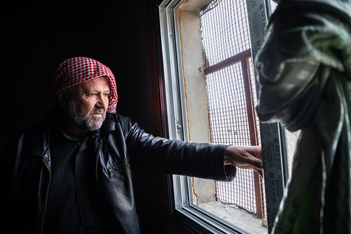 Un hombre con un pañuelo de cuadros rojos y blancos en la cabeza junto a una ventana