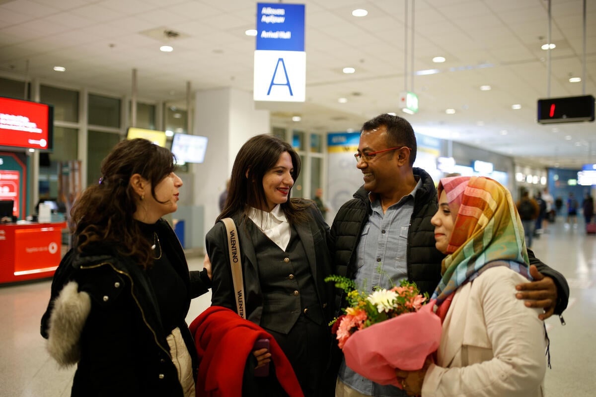 Tres mujeres y un hombre sonríen y se abrazan en un aeropuerto