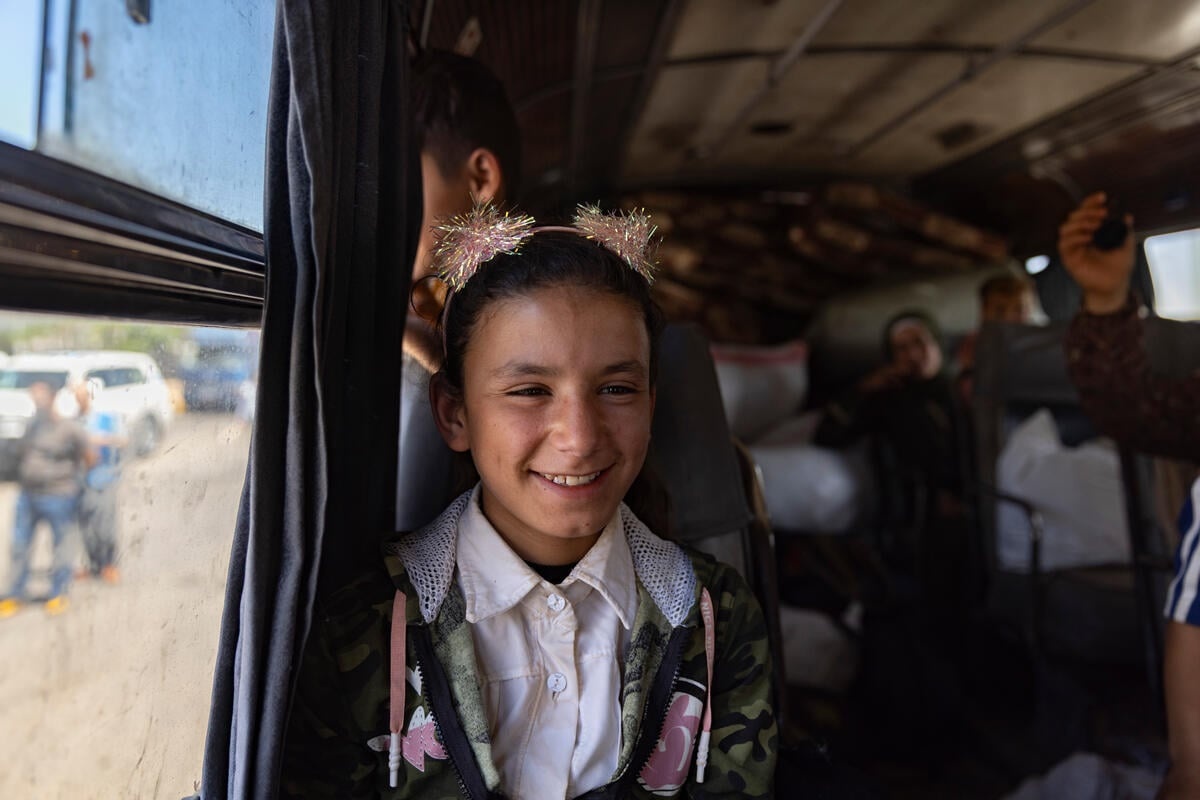 Una niña sonriente sentada junto a la ventanilla de un autobús