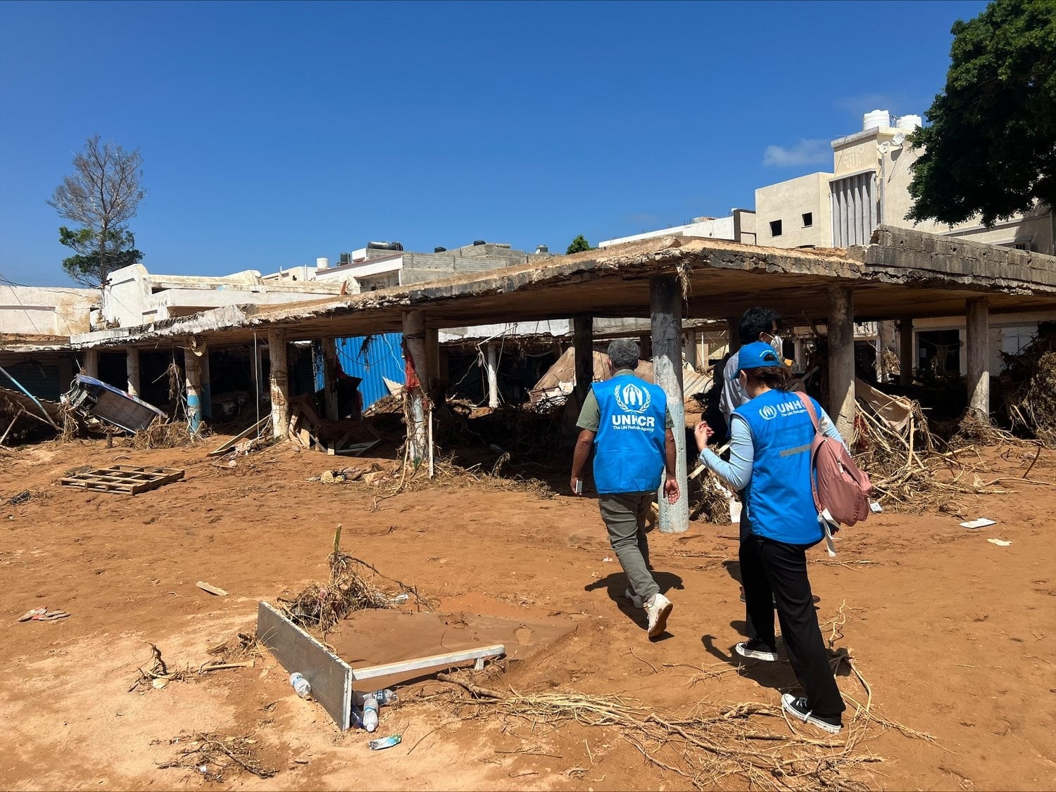 Dos trabajadores de ACNUR caminan frente a un edificio en ruinas