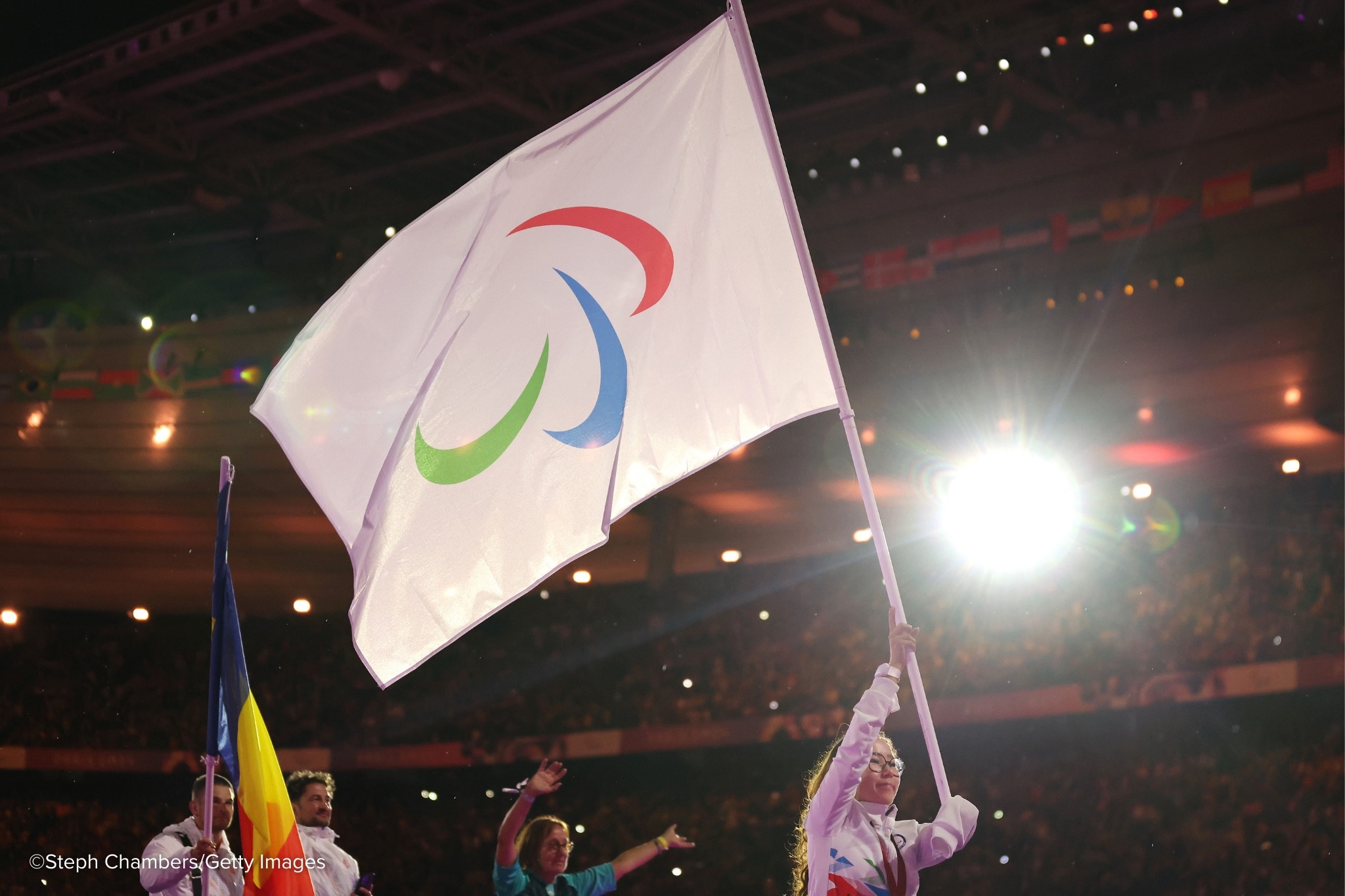 Una joven mujer lleva la bandera del IPC en un estadio iluminado.