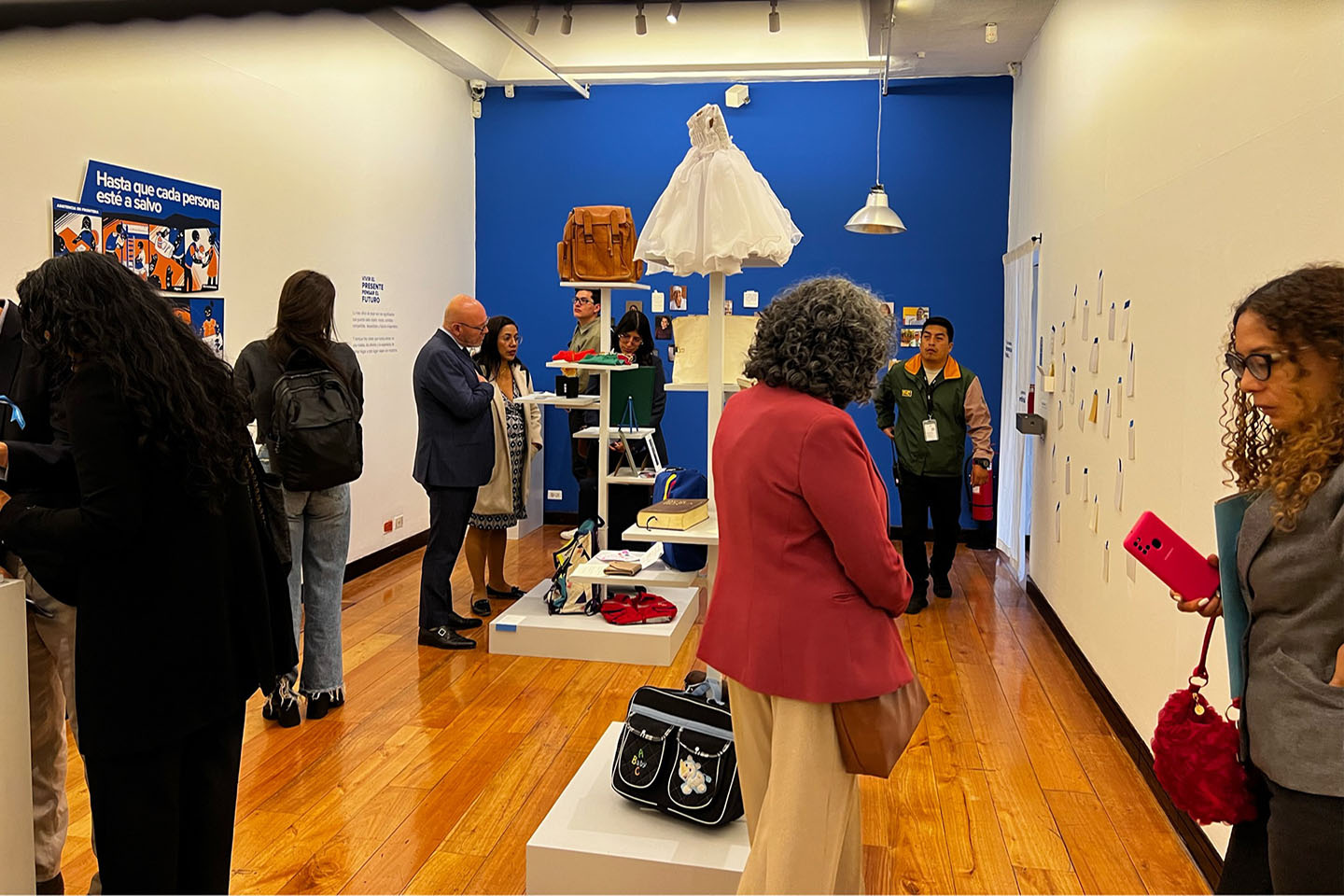 Varias personas miran una exposición de objetos personales como bolsos, cuadernos y ropa en una sala de museo.
