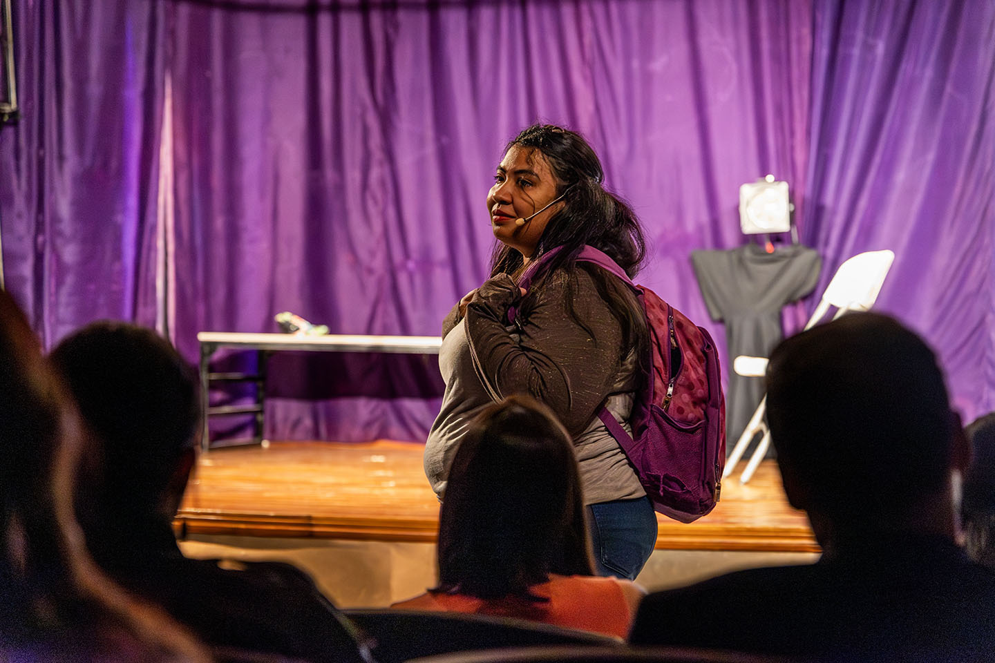 Una chica con una mochila actúa en una obra de teatro con expresión conmovida.