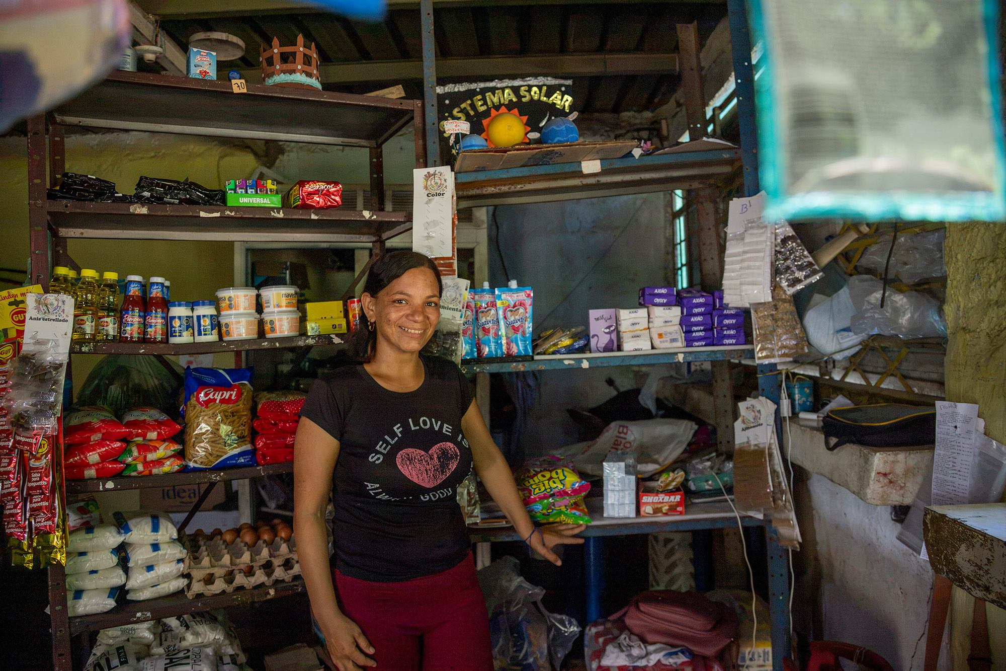 Una mujer vestida con camiseta negra y pantalón rojo, de pie dentro de una tienda de abarrotes