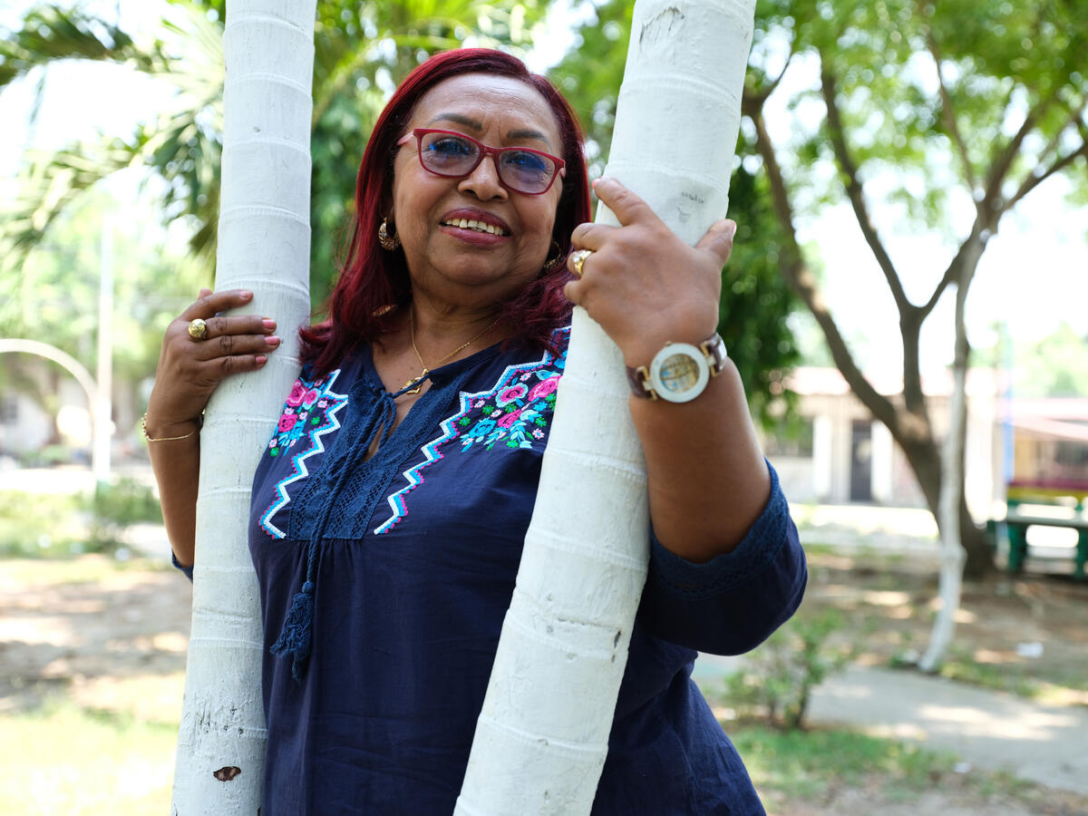 Una mujer con anteojos sonríe a la cámara abrazando una palmera