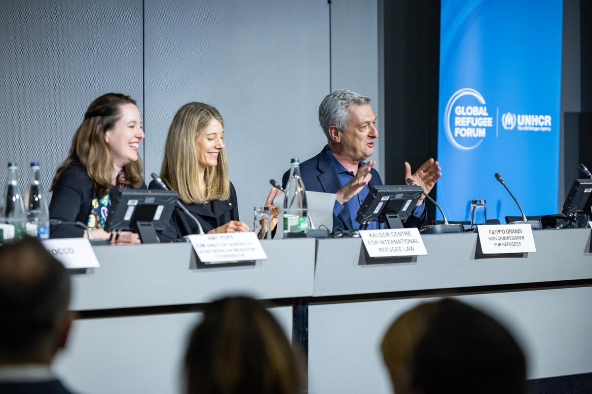 Dos mujeres de cabello rubio, y un hombre de cabello blanco, sentados en un panel.