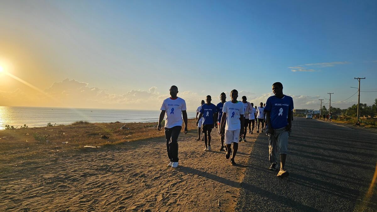 Un grupo de personas camina por una carretera junto a una playa al amanecer.