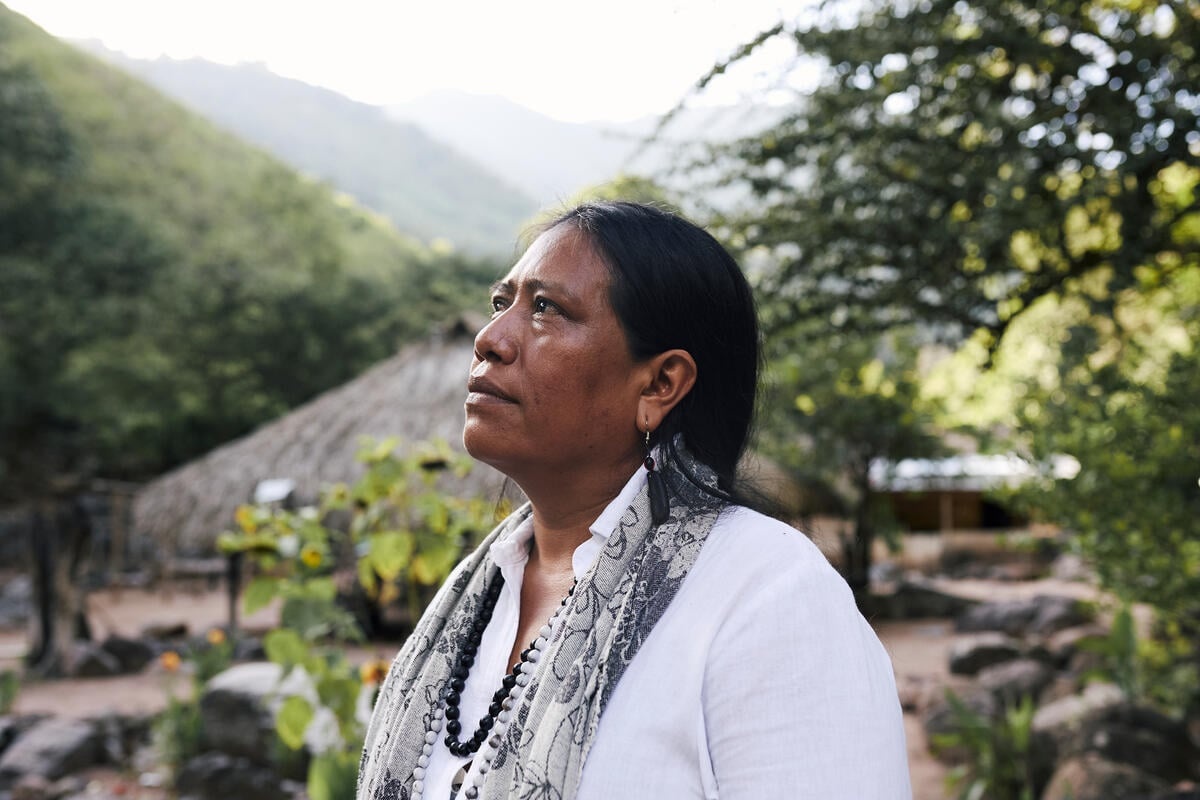 Una mujer vestida de blanco mira hacía el cielo en un ambiente rural.