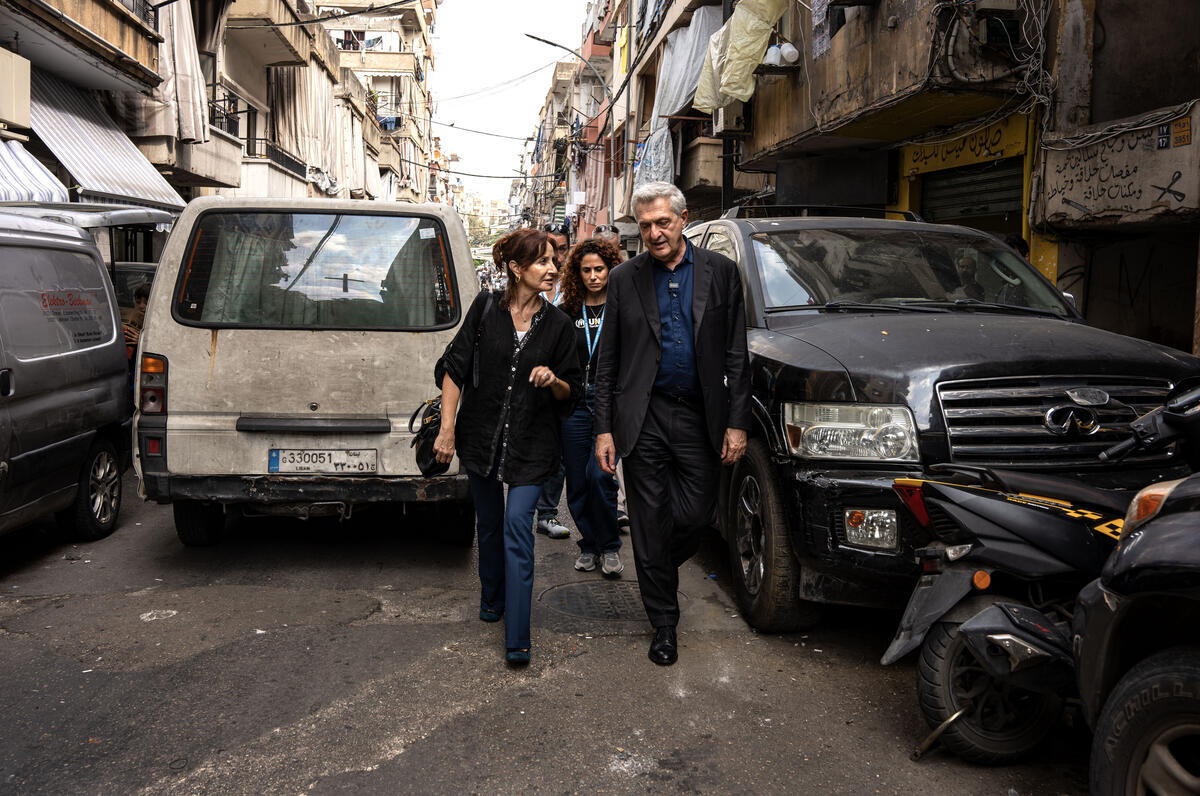 Dos mujeres y un hombre caminan entre vehículos estacionados en una estrecha calle de Beirut