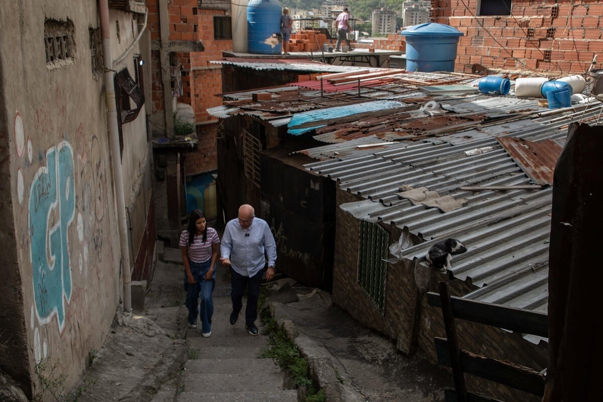 El Alto Comisionado recorre un callejón empinado en medio de casas de ladrillos y techos de zinc acompañado por Andriuska, una joven mujer, que camina a su lado.