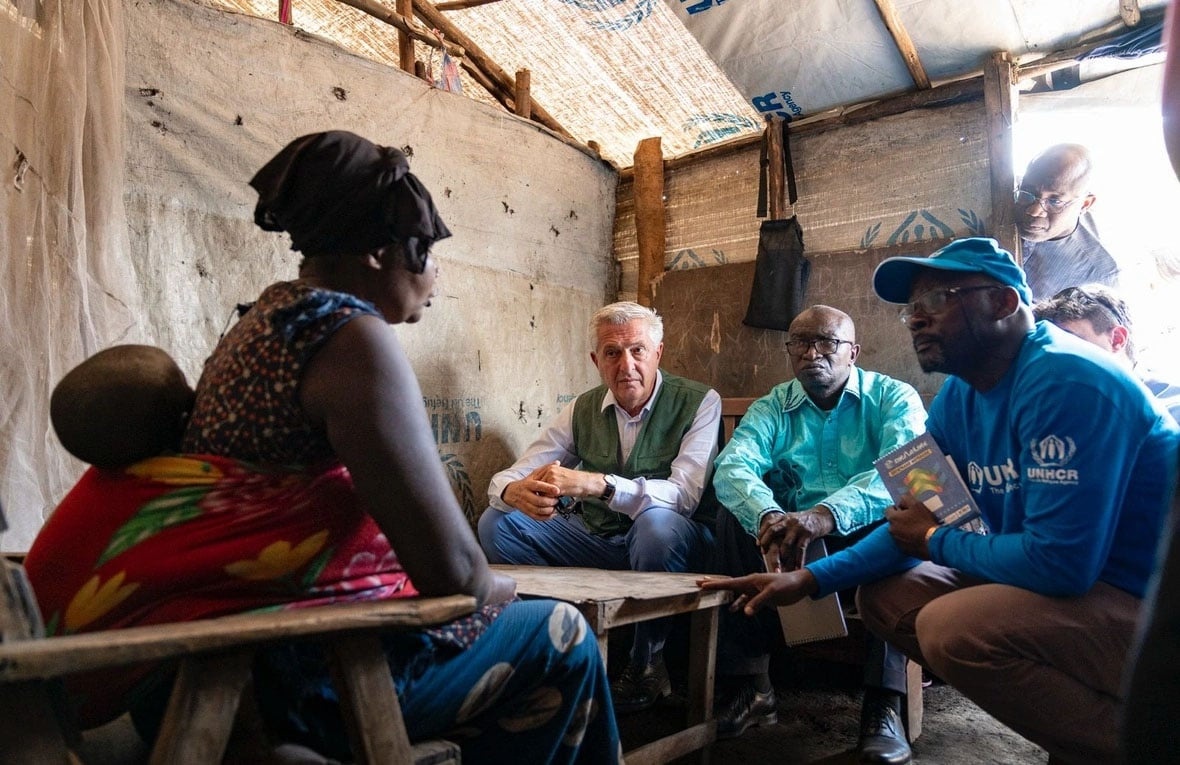 Personas conversan sentadas en un refugio provisional realizado con lonas de plástico y madera.