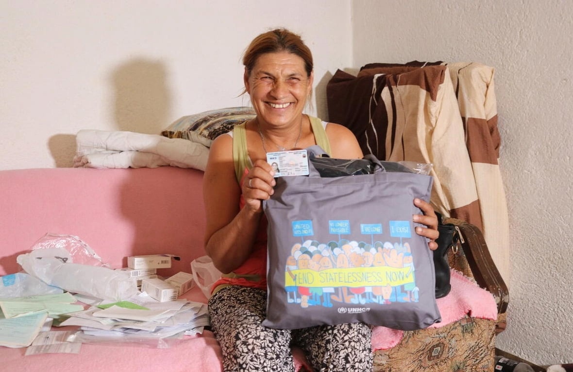 Una mujer sentada en una cama sostiene un bolsa gris y un documento de identidad