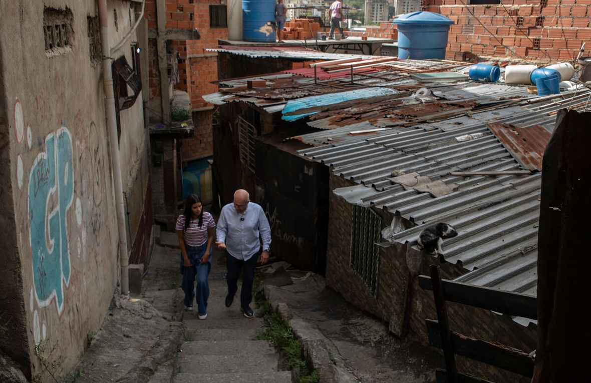 El Alto Comisionado recorre un callejón empinado en medio de casas de ladrillos y techos de zinc acompañado por Andriuska, una joven mujer, que camina a su lado.