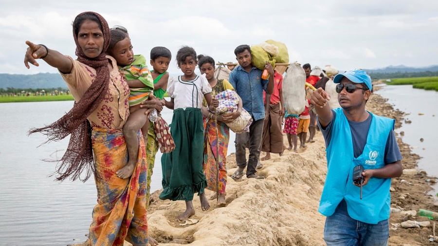 Una trabajadora de ACNUR le indica a un grupo de personas rohingyas refugiadas dónde se encuentra el centro de tránsito. 