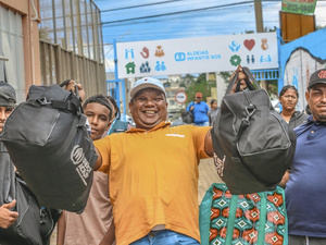 Un grupo de personas posa para la foto en la calle con al centro un hombre que muestra dos maletas sonriendo.